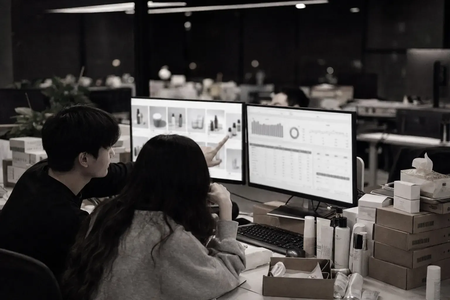 Two eCommerce operators at a desk in Hangzhou, one pointing at a screen of product listings