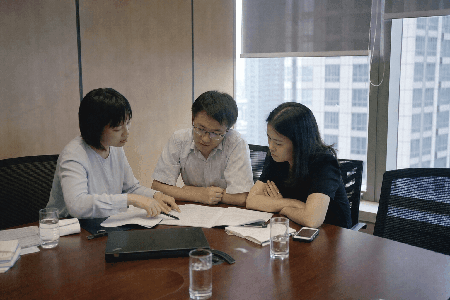 Three colleagues around the end of a meeting table, one pointing at a line in a printed document