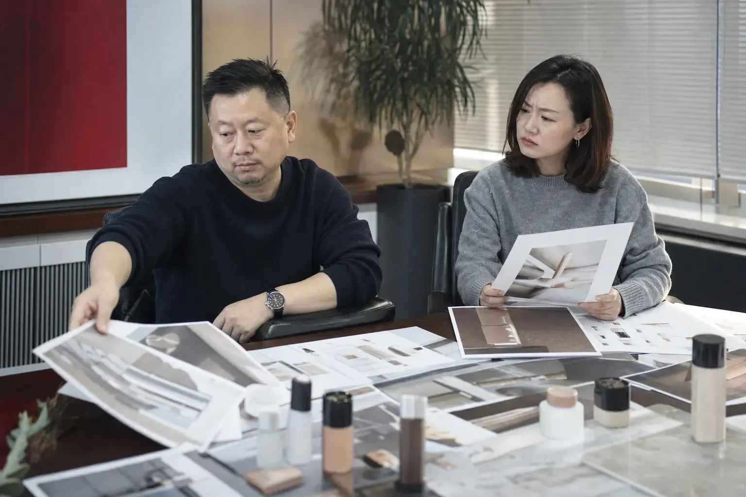 Two Chinese partners sorting through printed brand proposals and product samples, one of them looking skeptical