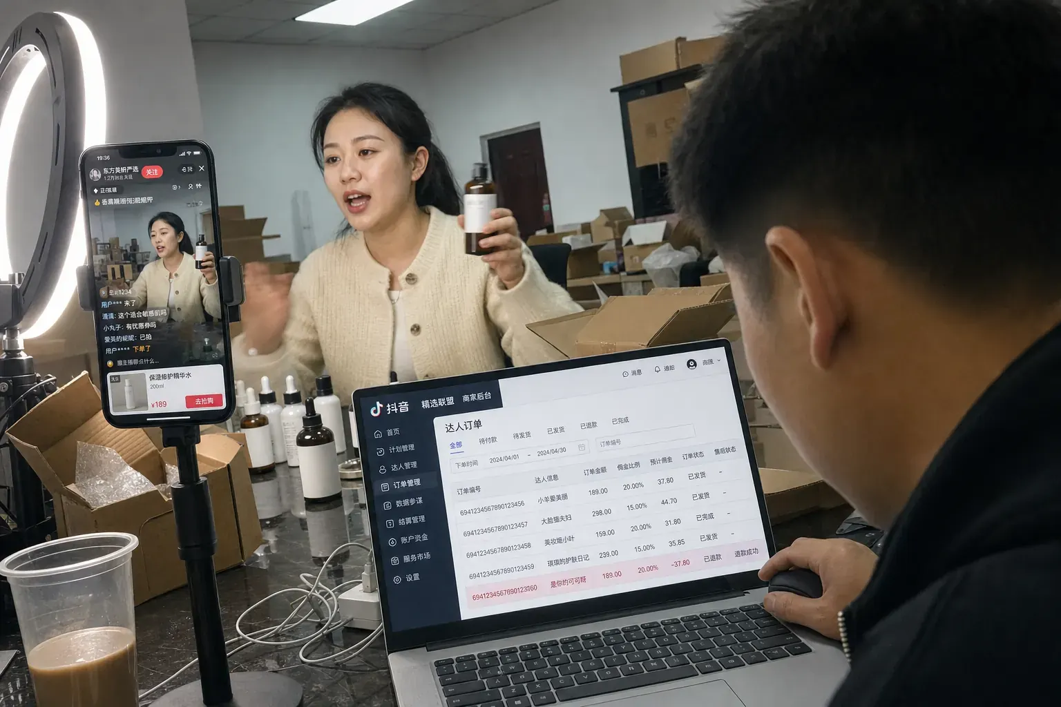 In a Linyi livestream base, a host holds a skincare bottle up to a phone on a tripod while a colleague checks Douyin creator orders on a laptop.