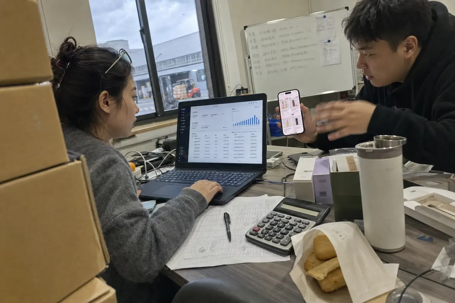 In a cross-border seller’s office in the Ningbo bonded zone, a woman reads a Douyin store payout page on a laptop while a colleague holds up a phone showing skincare product cards