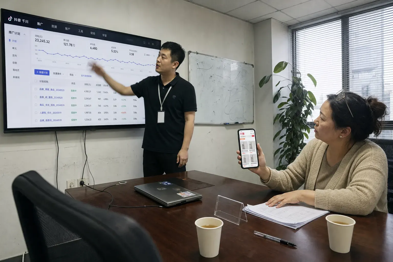 In a Nanjing agency meeting room, a man points at a Douyin Qianchuan ad dashboard on a wall screen while a woman across the table holds up a phone showing a Tmall store page.