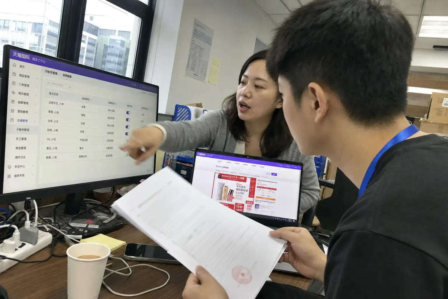 Two staff in a Guangzhou ecommerce office check a Tmall Global sub-account permissions screen while one holds a printed service contract