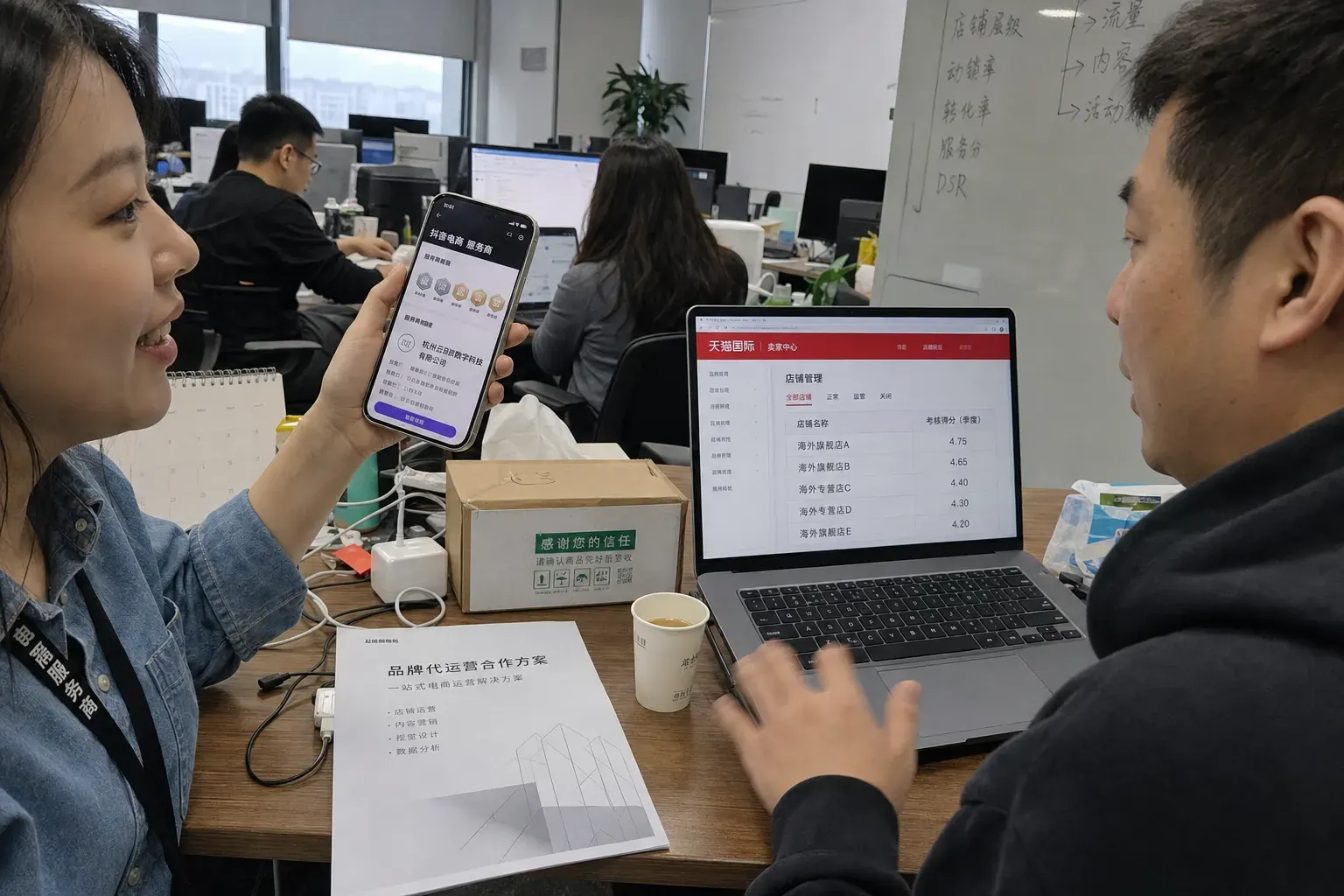 In a Hangzhou agency office, an e-commerce operator holds up a phone showing a Douyin service provider page with tier badges while a colleague reviews quarterly store scores in a Tmall Global seller backend.