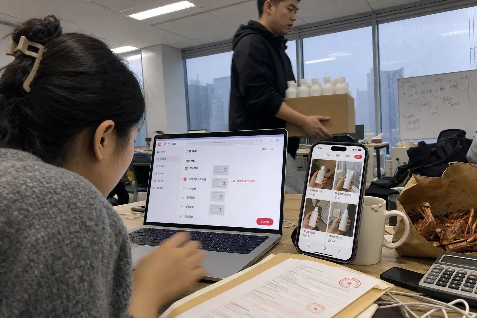 Im Büro eines E-Commerce-Dienstleisters in Chengdu prüft eine Mitarbeiterin am Laptop einen Shop-Antrag für RedNote, daneben zeigt ihr Smartphone ein Raster mit Produkt-Notes.